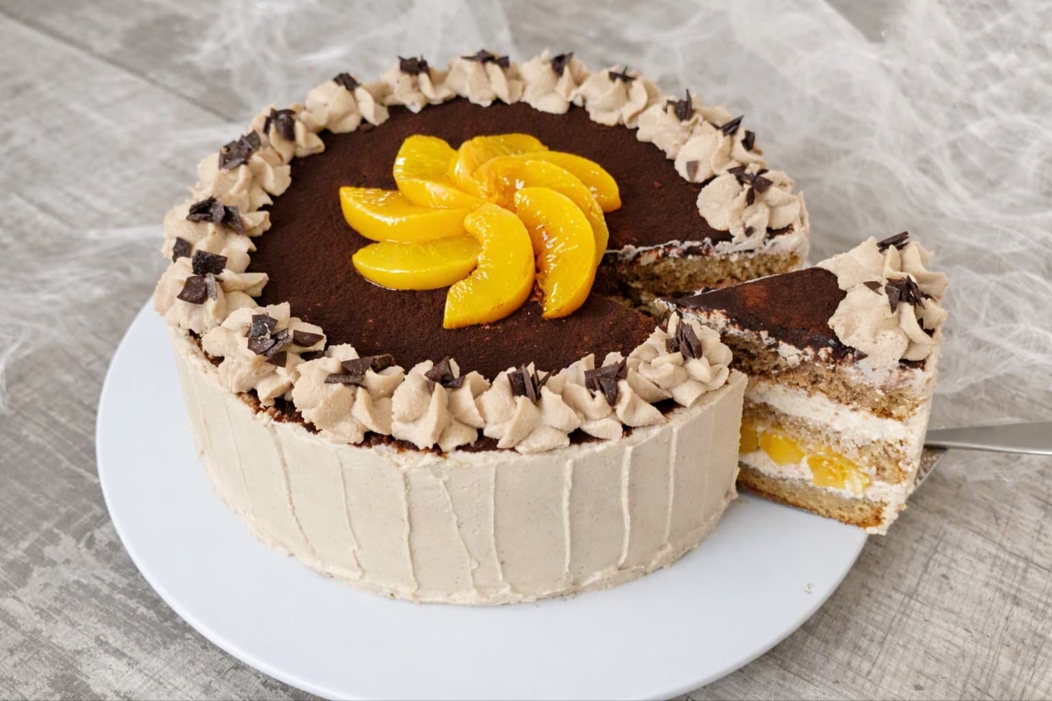 angeschnittene Kaffeetorte mit Kaffeecreme, Pfirsichschicht und Kakaotopping auf weißem Tortenteller