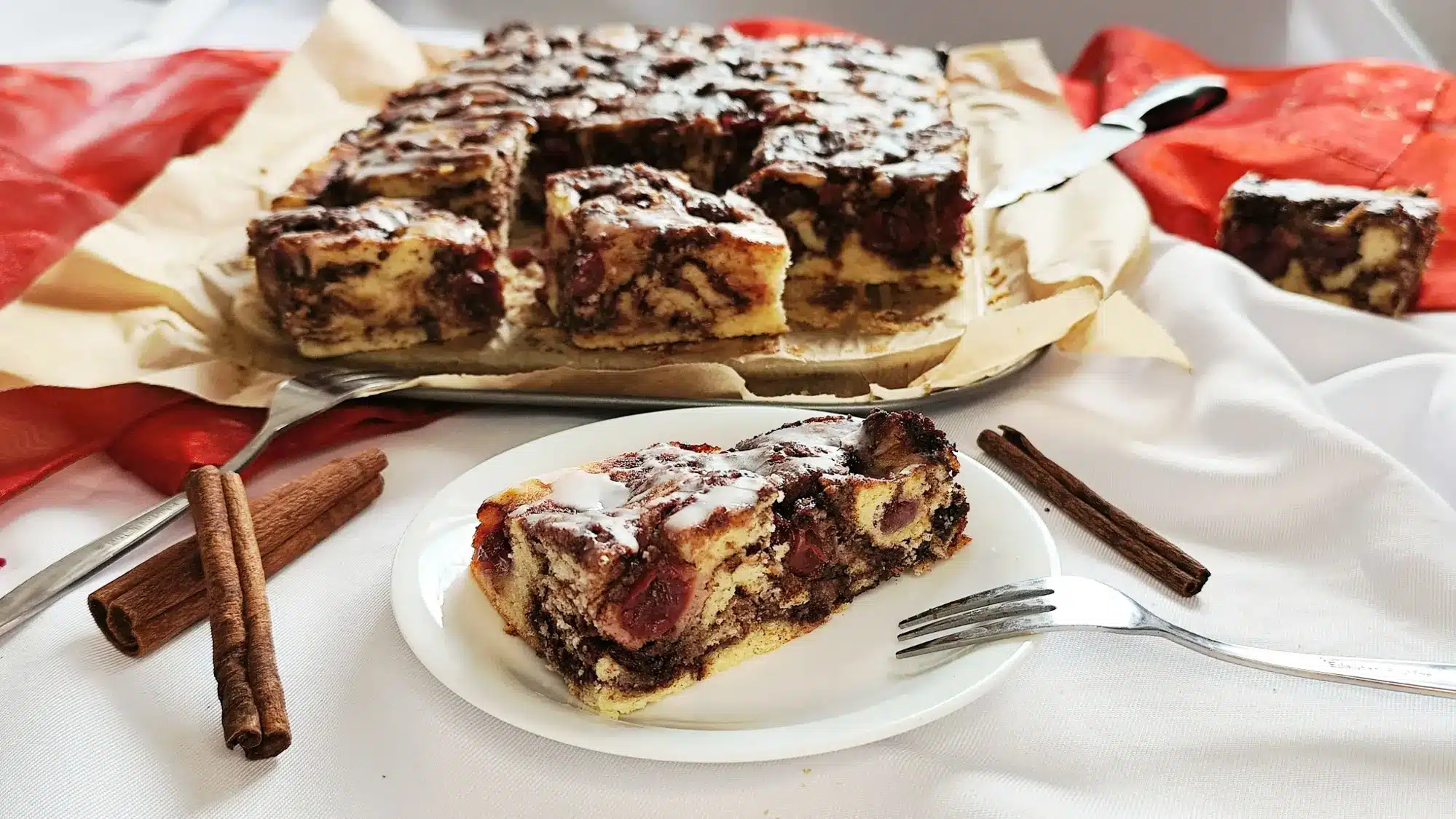 Frisch gebackener Zimt-Schneckenkuchen mit saftigen Kirschen ohne Hefe serviert auf einem Teller dekoriert mit Zimtstangen; ein winterlicher Kuchen mit weicher Schneckenstruktur