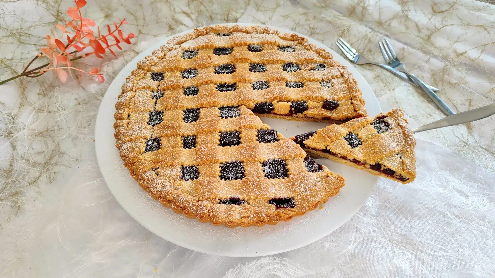 Fruchtige Tarte mit selbstgemachter Marmelade, Gitter aus Mürbeteig und Puderzucker, angeschnitten im Vordergrund