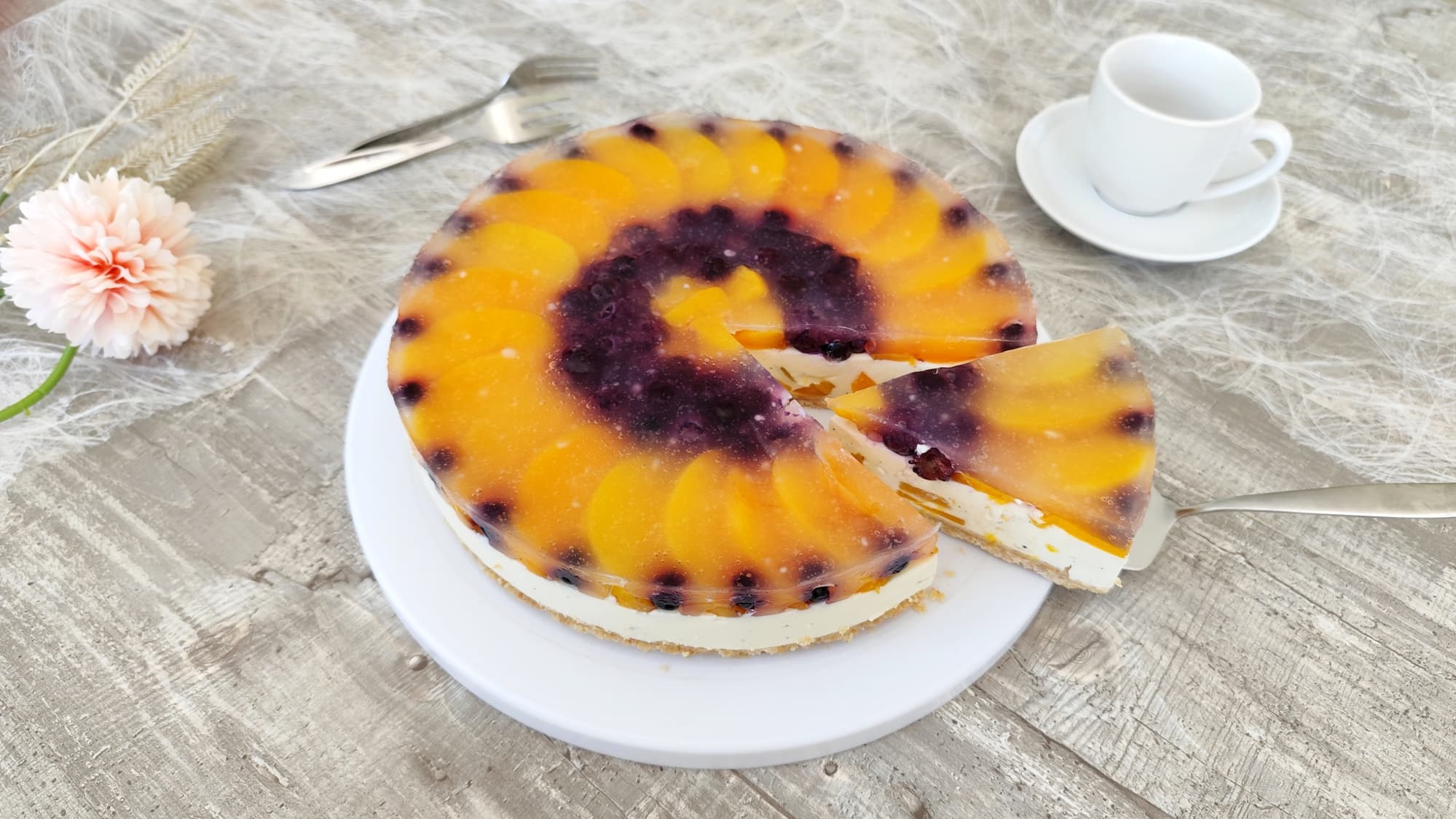 Panna Cotta Johurttorte mit Pfirsich auf Keksboden angeschnitten und serviert auf weißem Tortenteller
